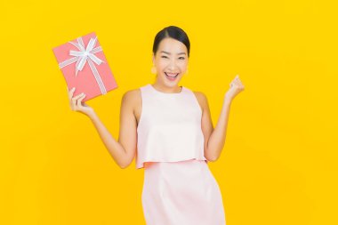 Asyalı güzel bir kadının portresi. Sarı arka planda kırmızı hediye kutusuyla gülümsüyor.