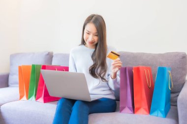 Güzel bir Asyalı kadının portresi evde online alışveriş için dizüstü bilgisayar kartı kullanıyor.