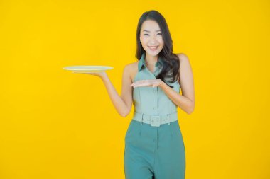 Güzel Asyalı bir kadının portresi. Arka planda boş tabak tabağıyla gülümsüyor.