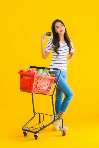 带有黄色背景信用卡的超级市场上漂亮的亚洲年轻女子购物车 — 图库照片
