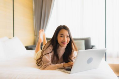 Yatak odasının iç kısmında dizüstü bilgisayar kullanan güzel Asyalı kadın portresi.