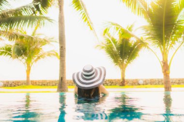 Güzel bir Asyalı kadın portresi, gün batımında palmiye ağacıyla birlikte havuz kenarında dinleniyor ya da tatil için gün doğumunda dinleniyor.