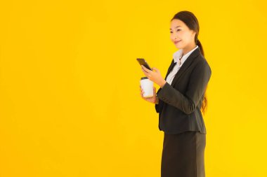 Portre güzel genç Asyalı kadın akıllı cep telefonu ve kahve fincanı ile izole edilmiş sarı arka planda