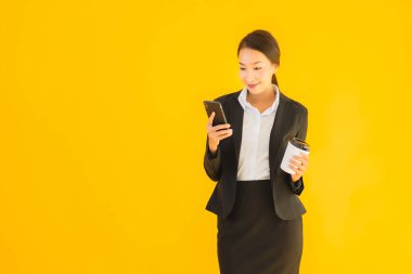 Portre güzel genç Asyalı kadın akıllı cep telefonu ve kahve fincanı ile izole edilmiş sarı arka planda