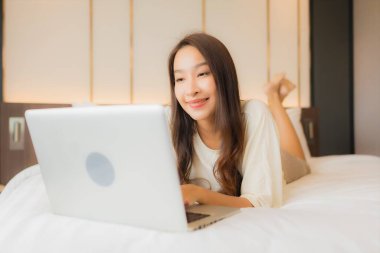Güzel bir Asyalı kadın yatak odasının içinde dizüstü bilgisayar kullanıyor.