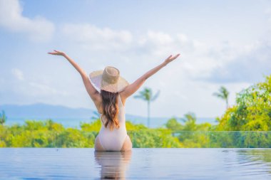 Güzel bir Asyalı kadın portresi gezide deniz manzaralı açık havuzda yüzüyor.