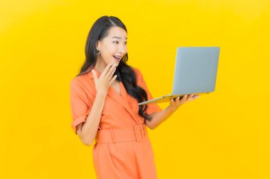 Asyalı güzel bir kadının portresi. Sarı izole edilmiş arka planda dizüstü bilgisayarla gülümsüyor.