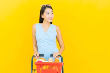 Asyalı güzel bir kadının portresi. Sarı arka planda süpermarketten alınmış alışveriş sepetiyle gülümsüyor.