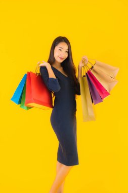 Sarı izole edilmiş arka planda renkli alışveriş çantalı güzel Asyalı kadın portresi.