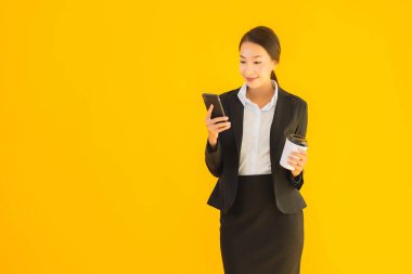 Portre güzel genç Asyalı kadın akıllı cep telefonu ve kahve fincanı ile izole edilmiş sarı arka planda