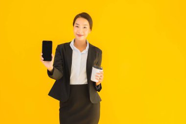 Portre güzel genç Asyalı kadın akıllı cep telefonu ve kahve fincanı ile izole edilmiş sarı arka planda