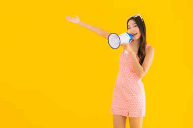Güzel bir Asyalı kadın, sarı izole edilmiş arka planda megafonla yüksek sesle konuşur.