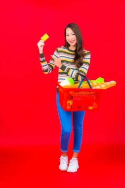 Marketten aldığı alışveriş sepetiyle kırmızı izole arka planda güzel bir Asyalı kadın portresi.