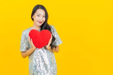 Asyalı güzel bir kadının portresi. Sarı arka planda kalp yastığı şeklinde gülümsüyor.