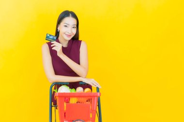 Renkli arka planda süpermarketten alınmış market sepetiyle gülümseyen güzel Asyalı kadın portresi.