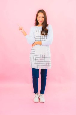 Portrait beautiful young asian woman in kitchen wear with apron on pink isolated background