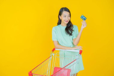 Renkli arka planda süpermarketten alınmış market sepetiyle gülümseyen güzel Asyalı kadın portresi.