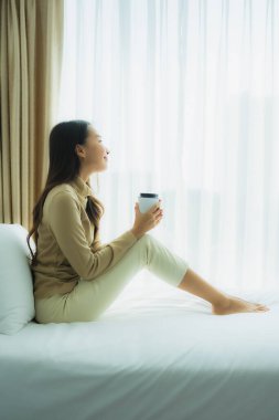 Yatak odasının iç tarafında, kahve fincanı olan Asyalı genç bir kadın.