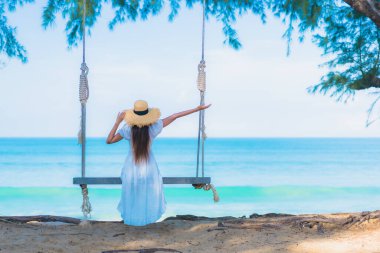 Güzel bir Asyalı kadın portresi gevşe, gülümse, deniz kıyısında sallan, mavi gökyüzü beyaz bulutuyla.