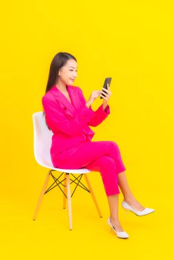 Güzel bir Asyalı kadın portresi sarı renkli izole edilmiş arka planda akıllı cep telefonu kullanır.