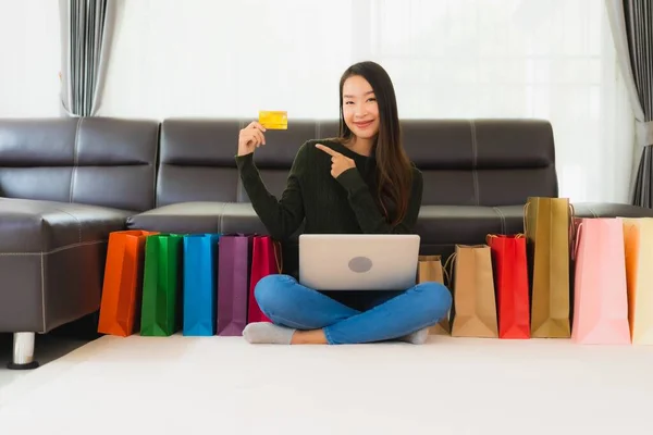 漂亮的年轻亚洲女人在家里用手提电脑和带有购物袋的信用卡进行网上购物 — 图库照片