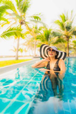 Güzel bir Asyalı kadın portresi, gün batımında palmiye ağacıyla birlikte havuz kenarında dinleniyor ya da tatil için gün doğumunda dinleniyor.