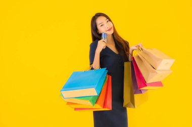 Portre güzel genç Asyalı kadın alışveriş çantası kredi kartı ve akıllı cep telefonu sarısı izole bir arka plan.