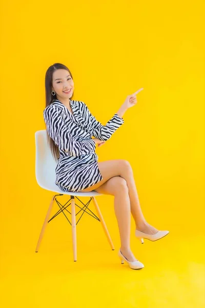 Portrait beautiful young asian woman sit on chair with action on yellow isolated background