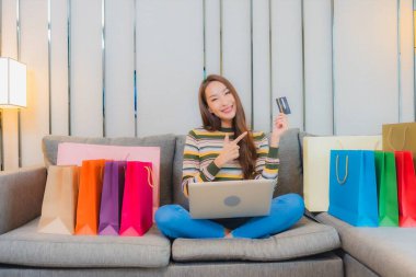 Asyalı güzel bir kadının portresi kanepeye dizüstü bilgisayar kullanıyor.