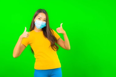 Güzel Asyalı genç bir kadının portresi, yeşil yalıtılmış arka planda kovid19 veya koronavirüsten korunmak için maske takar.