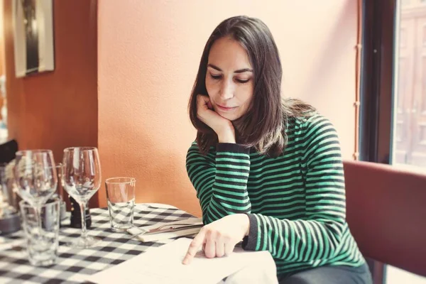 One attractive young lady sat at a table reading the menu in a bistro restaurant on her own