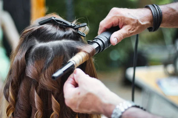 Back of the head of a young woman having her hair curled by a stylist using a curling iron