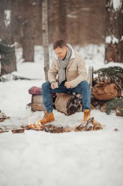Kış ormanında ateşin yanında bir adam kahve dolduruyor. Yüksek kalite fotoğraf