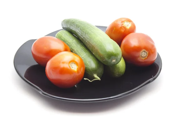 Frische grüne Gurken mit roten Tomaten auf schwarzem Keramikteller — Stockfoto