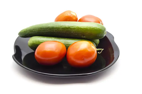 Frische grüne Gurken mit roten Tomaten auf schwarzem Keramikteller — Stockfoto