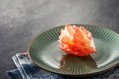 Yeşil bir yemek tabağına yerleştirilmiş kırmızı bir çiçek mermer bir zemin üzerinde