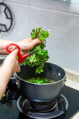 Bir şef sos yapıyor, tencereye doğranmış kişniş.