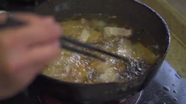 A chef is frying pork belly in a frying pan