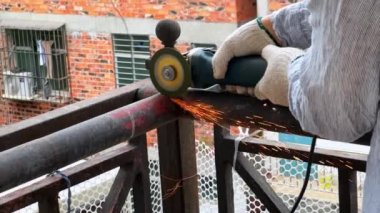 A worker is using a cutting machine to cut an iron guardrail to escalate in slow motion