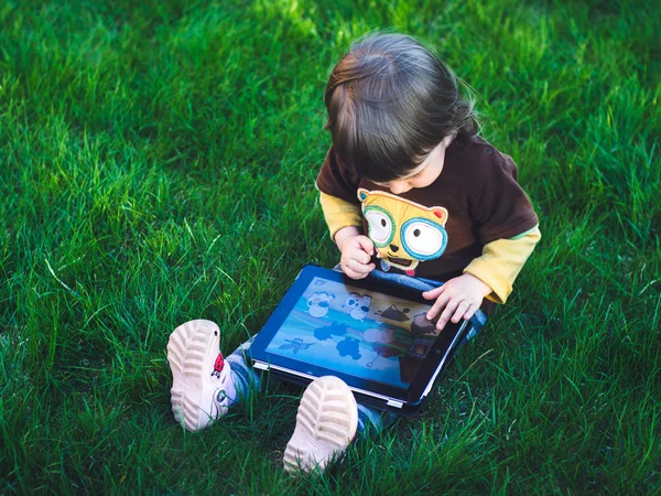 Çimenlerin üzerinde oturan ve bilgisayarı kullanan çocuk — Stok fotoğraf