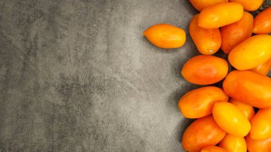 Bir sürü sarı, uzun meyveli domatesler gri taşlı arka planda