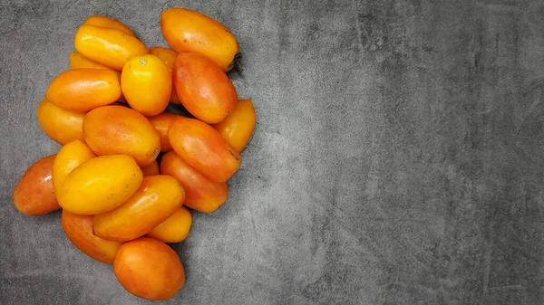 Viele gelb gestreckte langfruchtige Tomaten auf grauem Steinhintergrund — Stockfoto