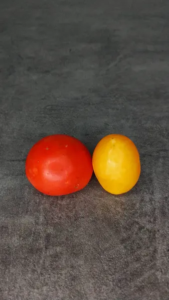 Ein Paar verschiedene Tomaten auf grauem Steingrund. Gelbe längliche und rote runde Tomaten. — Stockfoto