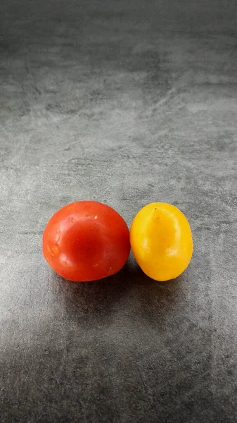 Ein Paar verschiedene Tomaten auf grauem Steingrund. Gelbe längliche und rote runde Tomaten. — Stockfoto