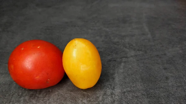 Пара различных помидоров на сером каменном фоне. Желтые продолговатые и красные круглые помидоры. — стоковое фото