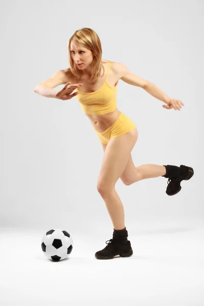 Jong meisje in geel gaat te schoppen van een bal — Stockfoto