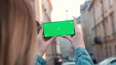Lviv, Ukraine - May 6, 2022: Close up Horizontal hands holding smartphone with green screen outside. Green screen mobile phone with chroma key. Perfect for product placement