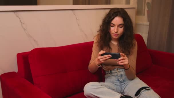 Young women listening to music and dancing energetic and rhythm at couch. Attractive Asian girl looking at the smart phone sitting in the living room spending leisure time at home. — Αρχείο Βίντεο