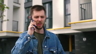 Ciddi yüzlü yakışıklı beyaz adam şehir merkezindeki iş hakkında cep telefonuyla konuşuyor. Açık havada. Yüksek kalite 4k görüntü