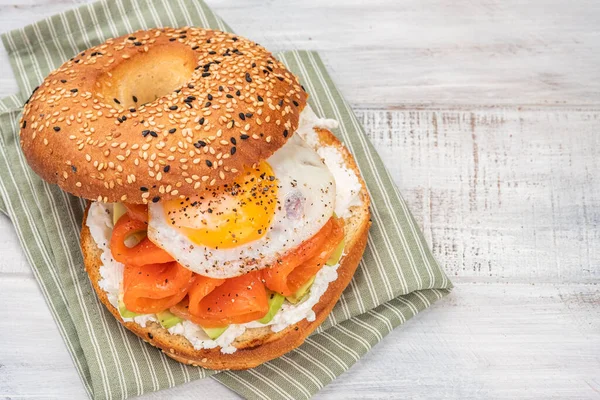 Bagel szendvics lazaccal, krémsajttal, avokádóval és tojással. Stock Fotó